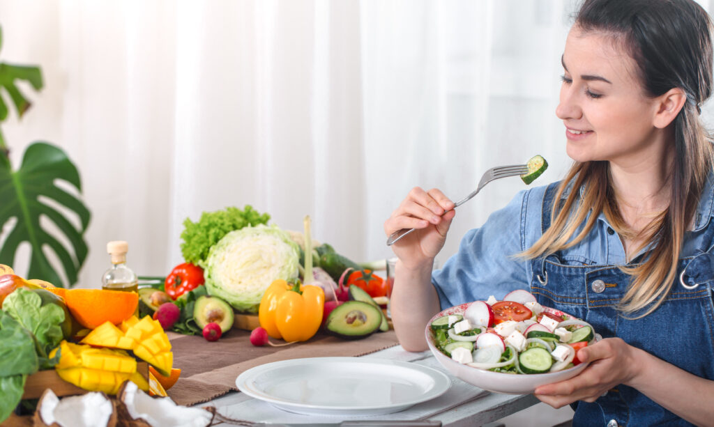 Jeune-femme-heureuse-mangeant-une-salade-et-des-légumes-bio-table-fond-clair