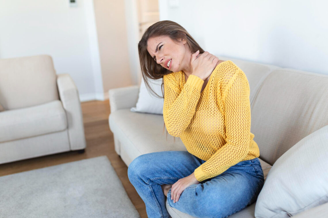 Femme assise sur un canapé portant la main à son coup