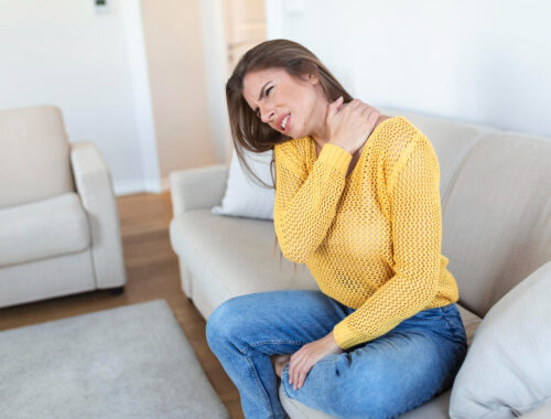 Femme assise sur un canapé portant la main à son coup