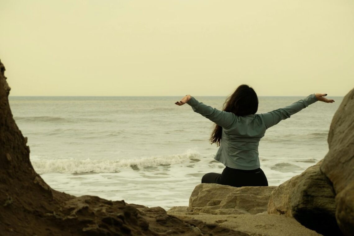 Femme les bras grands ouverts au coucher du soleil profitant d'un moment de sérenité.