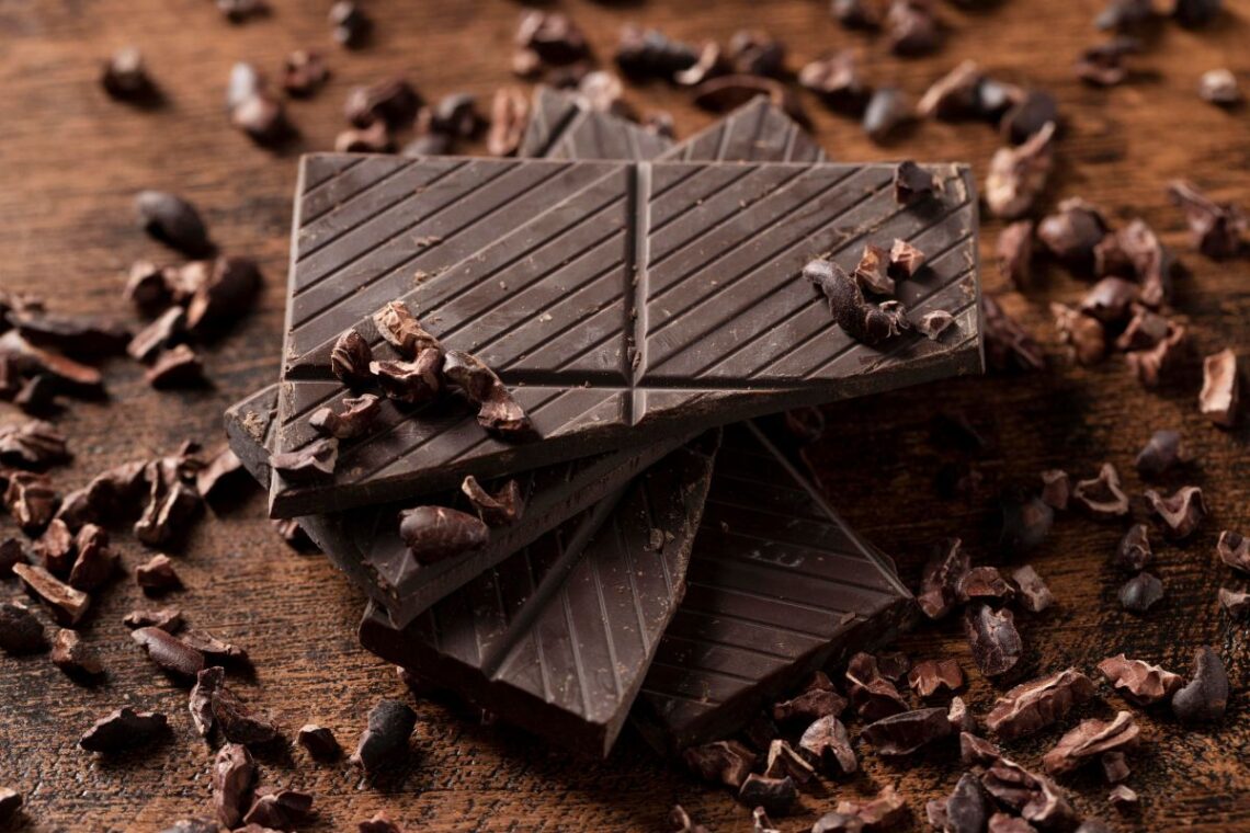 Carrés de chocolat noir posés sur une planche en bois, avec éclats de cacao, illustrant la sophro-dégustation.