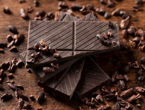 Carrés de chocolat noir posés sur une planche en bois, avec éclats de cacao, illustrant la sophro-dégustation.