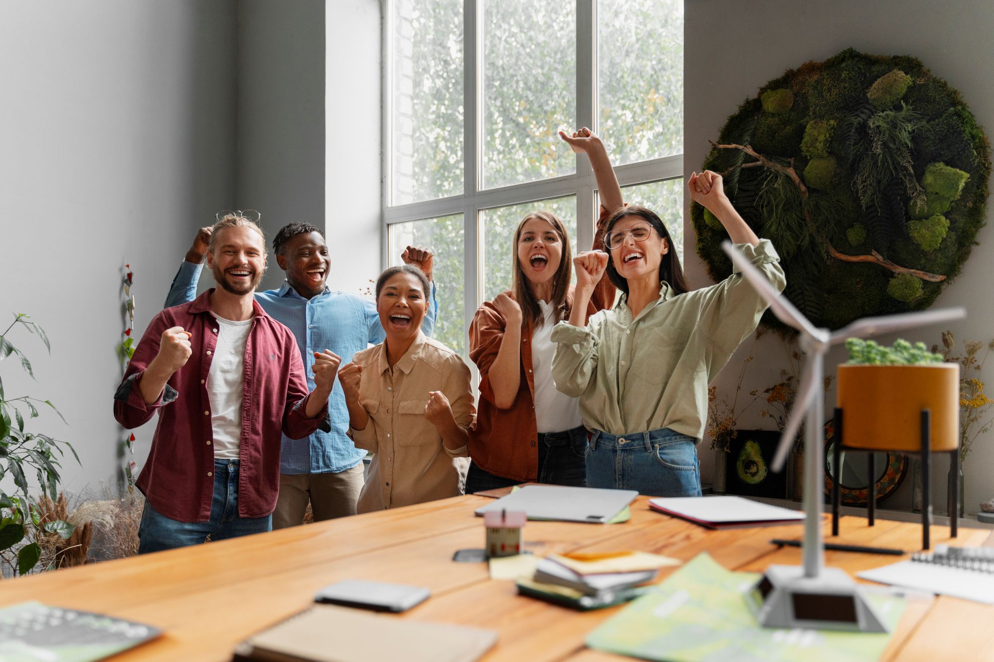 Une équipe enthousiaste collabore dans un espace lumineux et naturel, autour d’un projet créatif lié au bien‑être et à l’innovation. Une photo inspirante qui illustre l’énergie positive, la coopération et l’engagement dans un environnement professionnel apaisant.